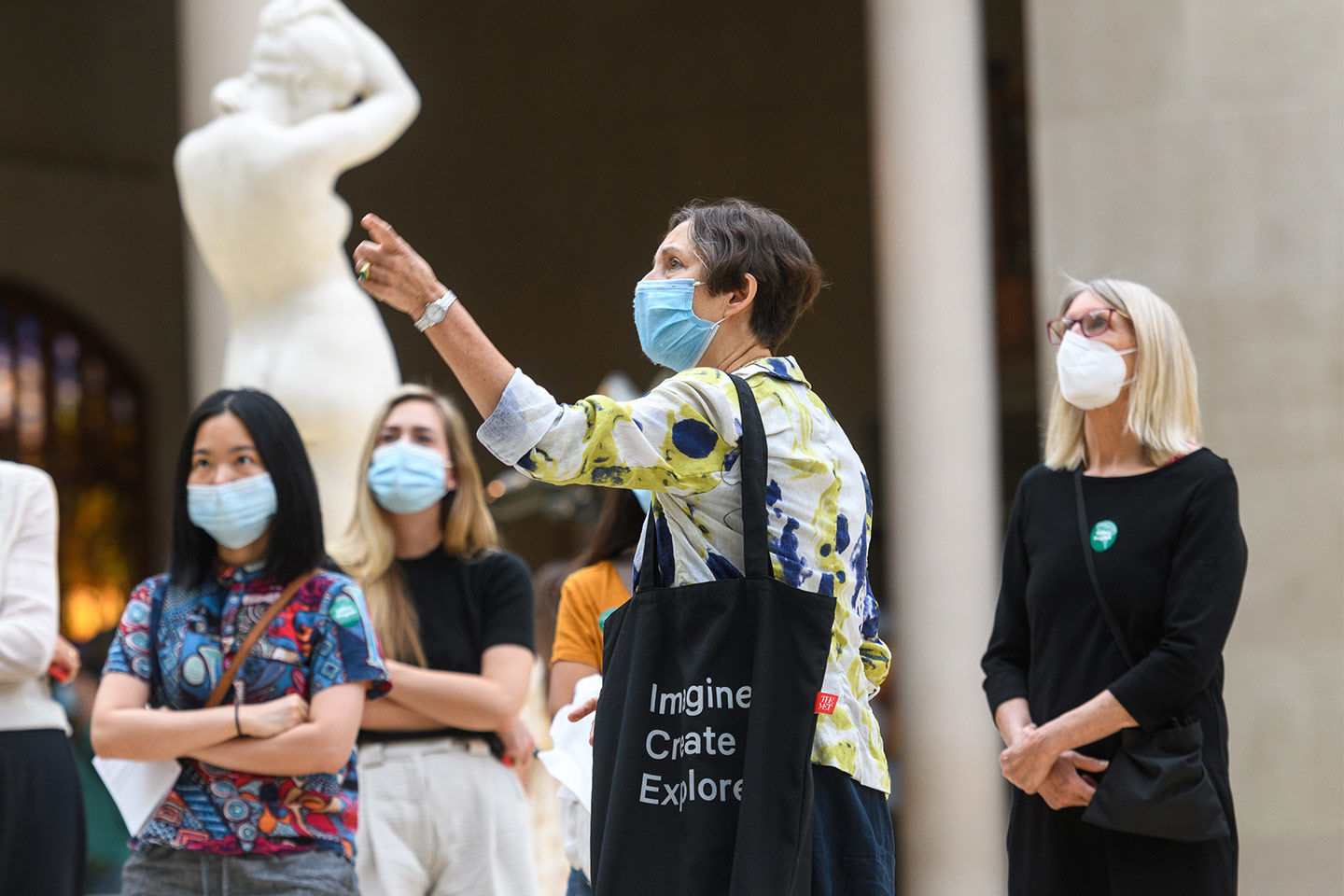 One woman points as a group of people stand inside a gallery looking at a sculpture